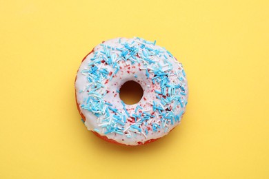 Photo of Glazed donut decorated with sprinkles on yellow background, top view. Tasty confectionery
