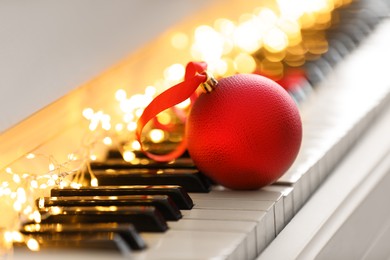 Photo of Beautiful red bauble and fairy lights on piano keys, closeup. Christmas music