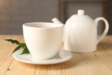 Photo of Cup and teapot on light wooden table, closeup