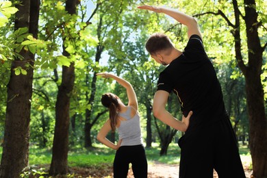 Man and woman doing morning exercise in park, back view