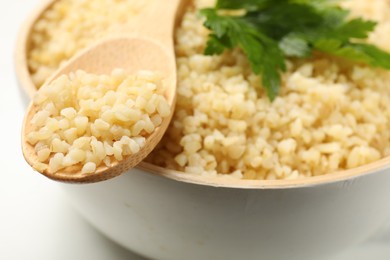 Delicious bulgur with parsley and spoon on table, closeup