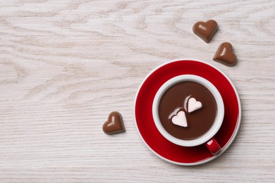 Cup of hot chocolate with heart shaped marshmallows and tasty candies on white wooden table, flat lay. Space for text