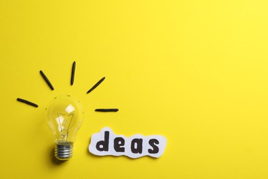 Word Ideas made with lightbulb and paper sheet on yellow background, flat lay. Space for text