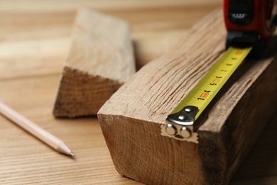 Photo of Tape measure, timber strips and pencil on wooden table, closeup