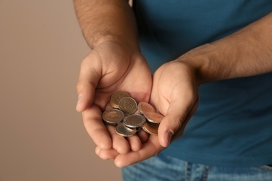 Photo of Young man with handful of coins on beige background, closeup