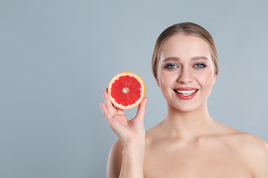 Photo of Young woman with cut grapefruit on grey background, space for text. Vitamin rich food