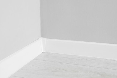 White plinth with connector on laminated floor near wall indoors, closeup