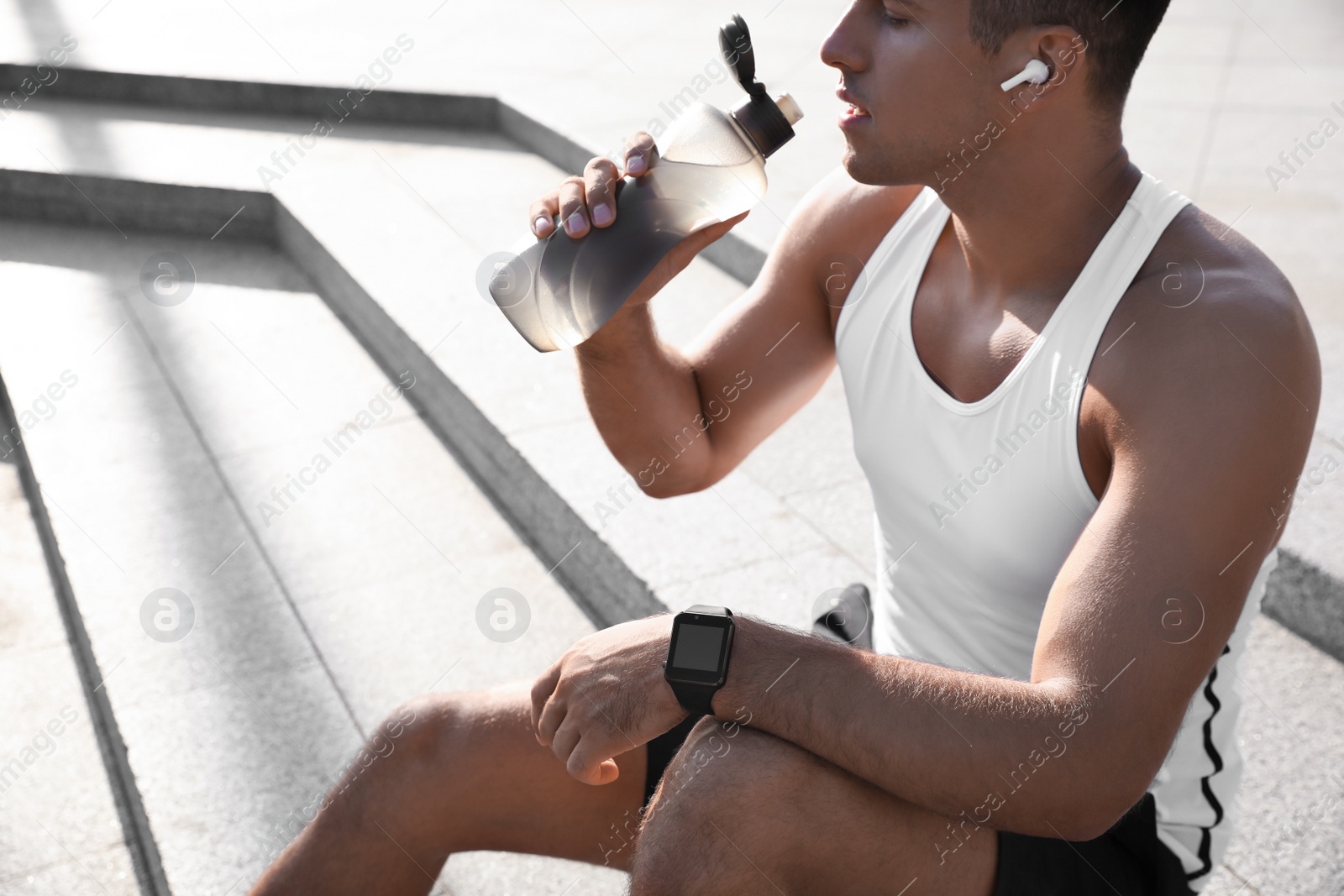 Photo of Man with fitness tracker drinking water after training outdoors, closeup