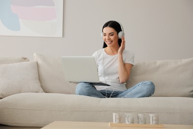 Woman with laptop and headphones sitting on sofa at home