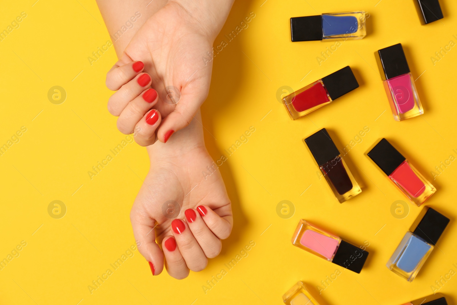 Photo of Woman with red manicure and nail polish bottles on color background, top view