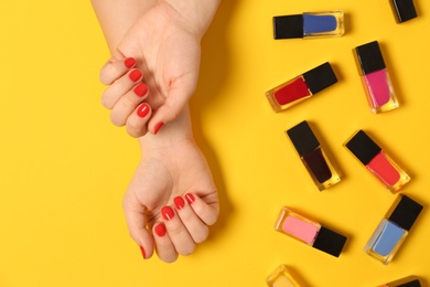 Woman with red manicure and nail polish bottles on color background, top view