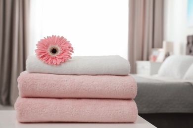 Photo of Stack of clean towels with flower on table in bedroom