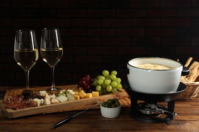 Photo of Fondue with tasty melted cheese, forks, different snacks and wine on wooden table