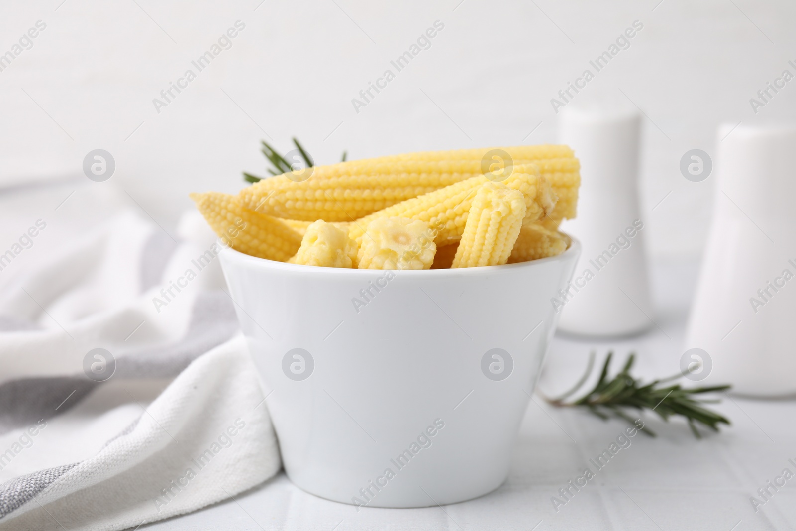 Photo of Tasty fresh yellow baby corns in bowl on white tiled table