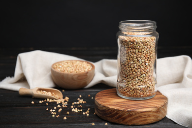 Photo of Jar with green buckwheat on black wooden table. Space for text