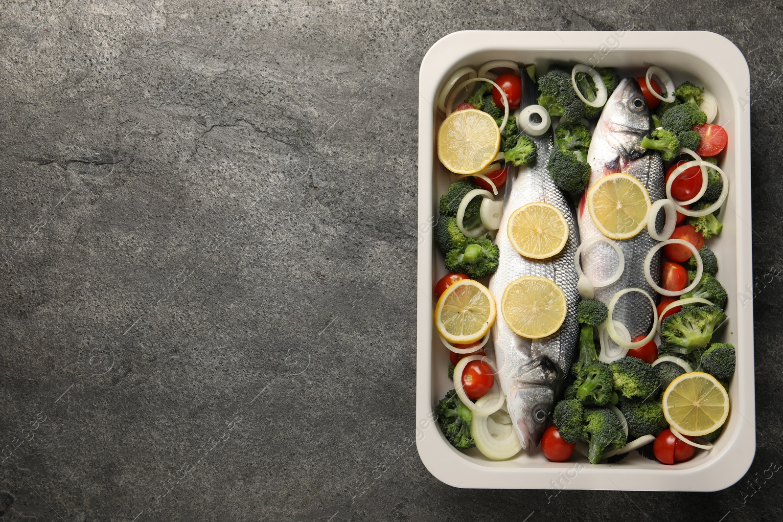 Photo of Raw fish with vegetables and lemon in baking dish on grey textured table, top view. Space for text