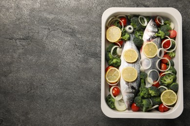 Photo of Raw fish with vegetables and lemon in baking dish on grey textured table, top view. Space for text