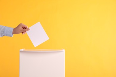 Photo of Woman putting her vote into ballot box on orange background, closeup. Space for text