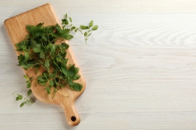 Photo of Fresh stinging nettle leaves on white wooden table, flat lay. Space for text