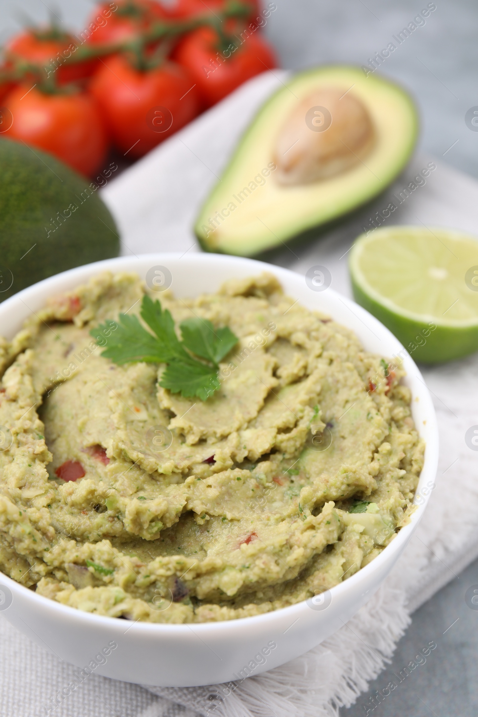 Photo of Bowl of delicious guacamole and ingredients on grey table, closeup