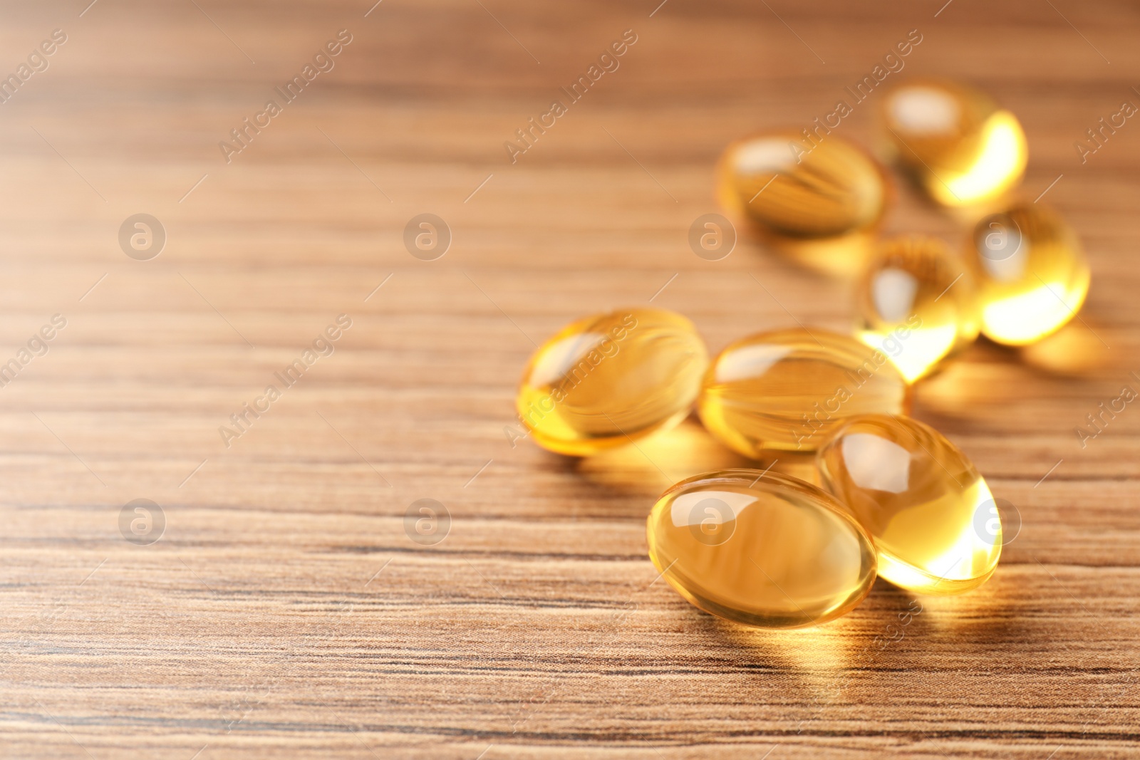 Photo of Dietary supplement capsules on wooden table, closeup. Space for text