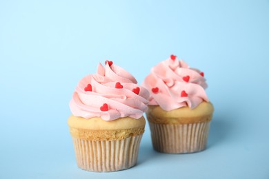 Photo of Tasty cupcakes with heart shaped sprinkles for Valentine's Day on light blue background