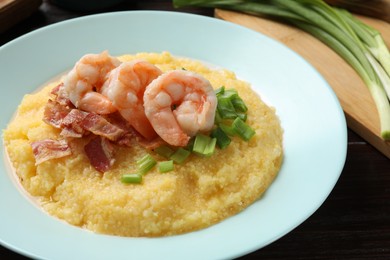 Photo of Plate with fresh tasty shrimps, bacon, grits and green onion on dark wooden table, closeup