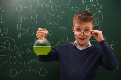 Schoolboy holding flask near chalkboard with chemical formulas