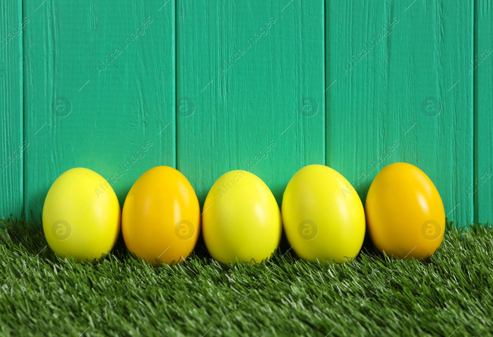 Photo of Bright Easter eggs on green grass against wooden background