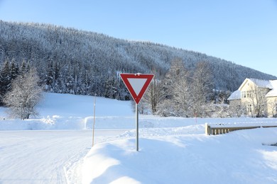 Traffic sign Give Way near road covered with snow on winter day