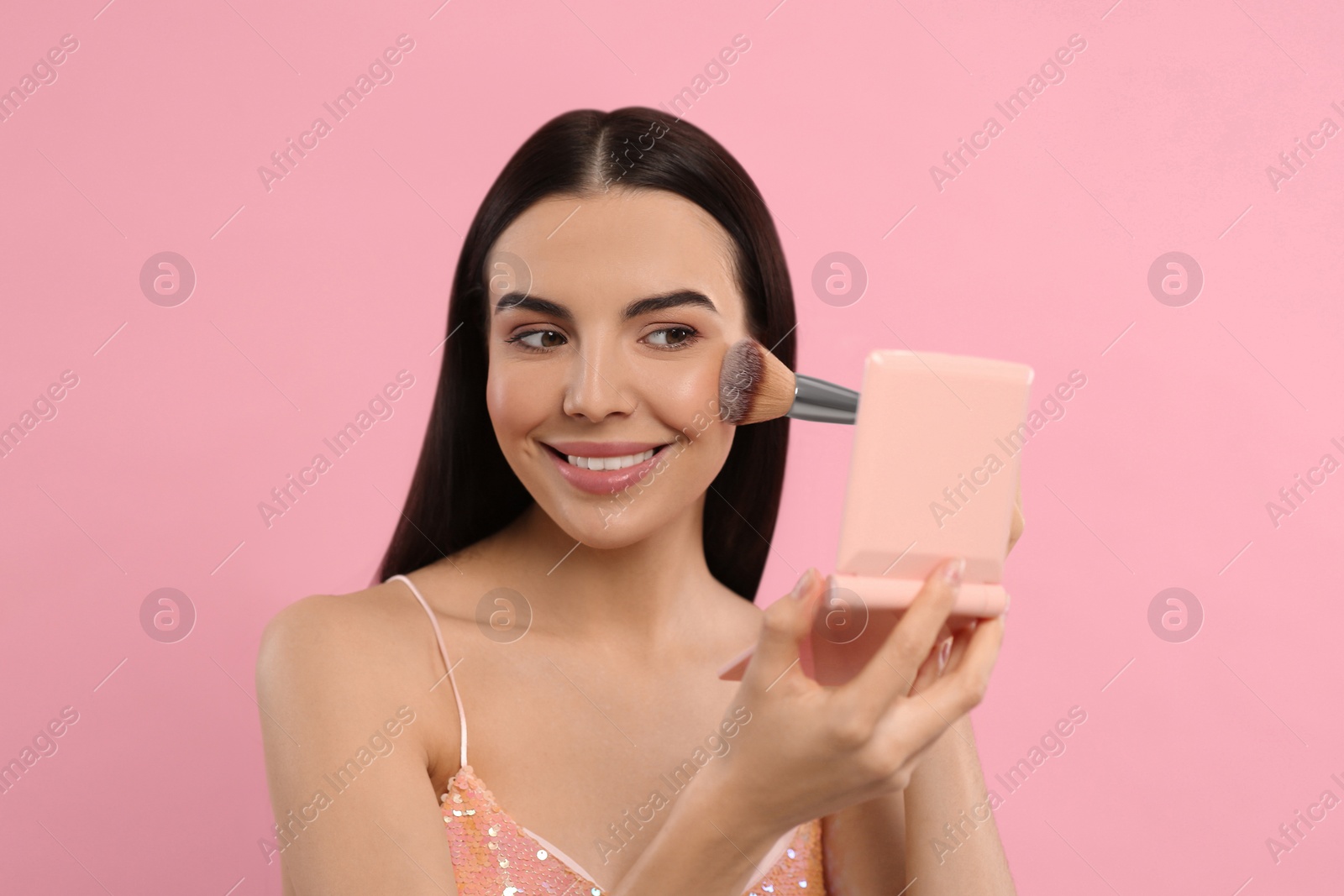 Photo of Beautiful woman with cosmetic pocket mirror applying makeup on pink background