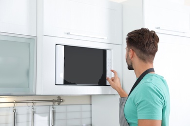 Photo of Young man using modern microwave oven at home