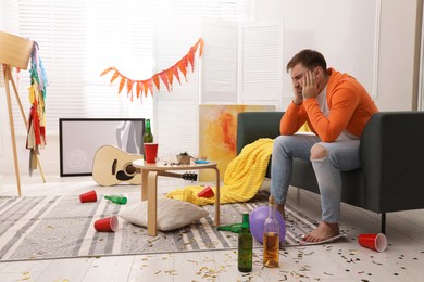 Photo of Tired drunk man on sofa in messy room after party