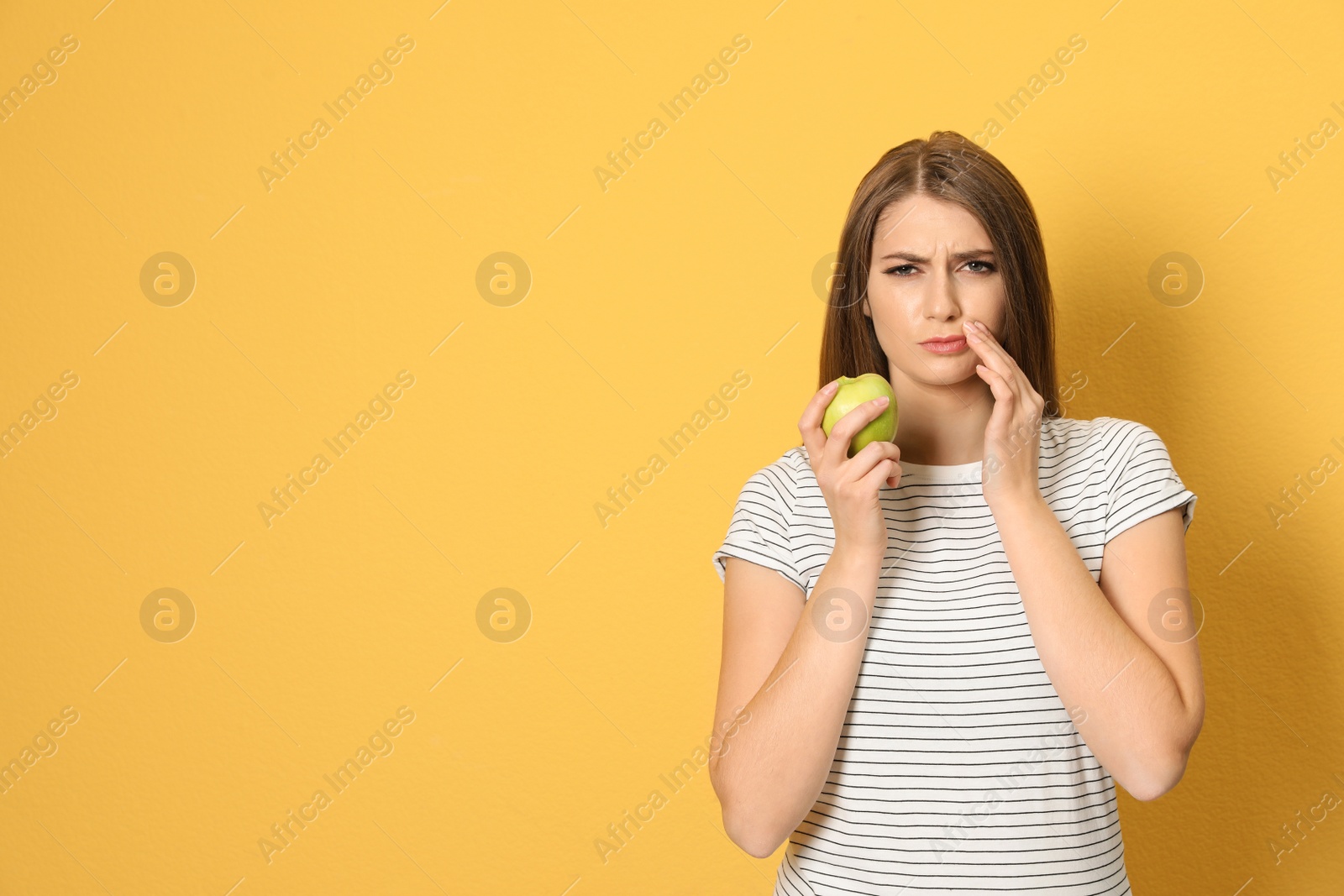 Photo of Emotional young woman with sensitive teeth and apple on color background. Space for text