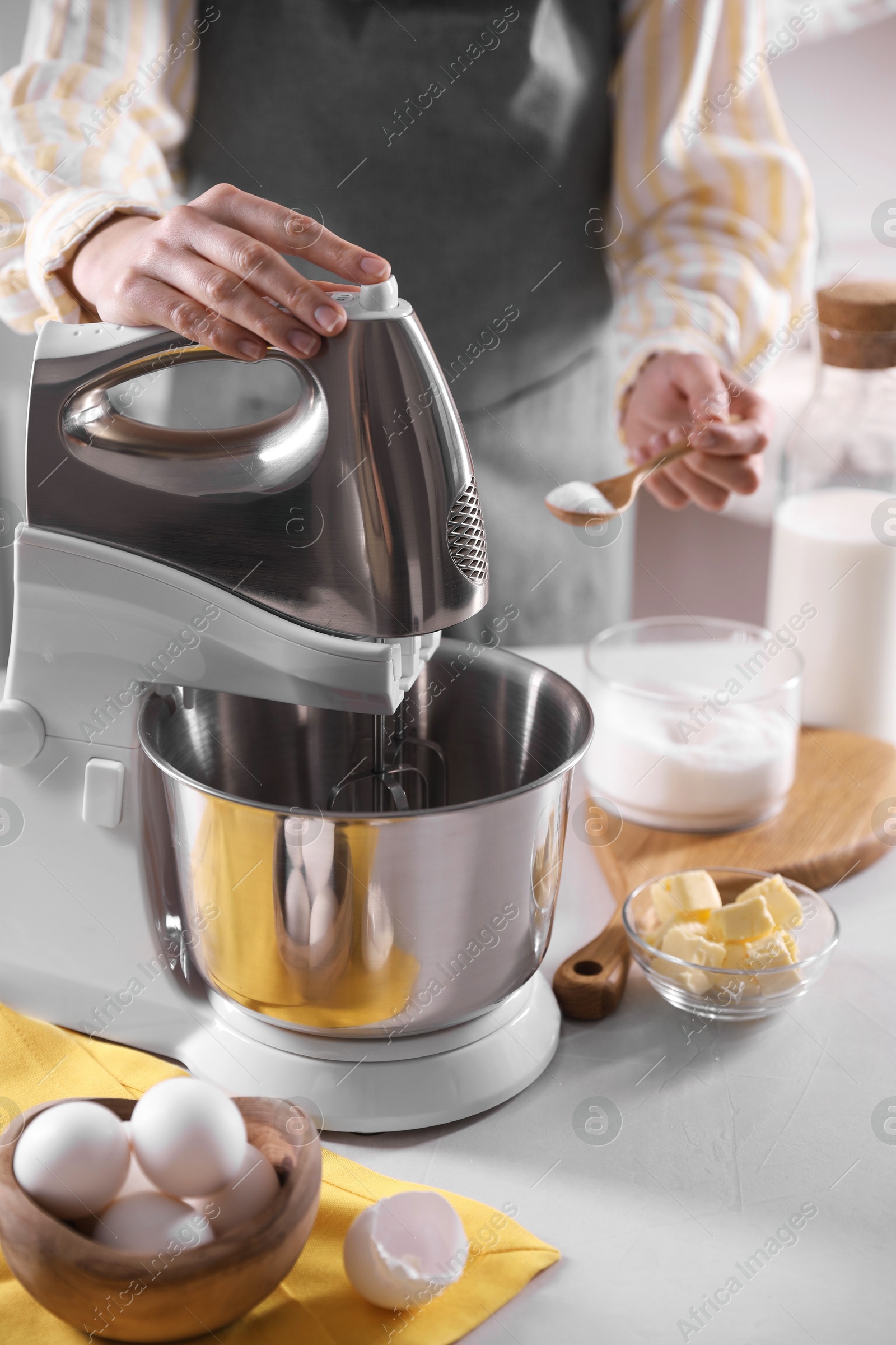 Photo of Woman adding sugar into bowl of stand mixer while making dough at table indoors, closeup