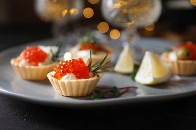 Delicious tartlets with red caviar, cream cheese and lemon served near wine on black table, closeup