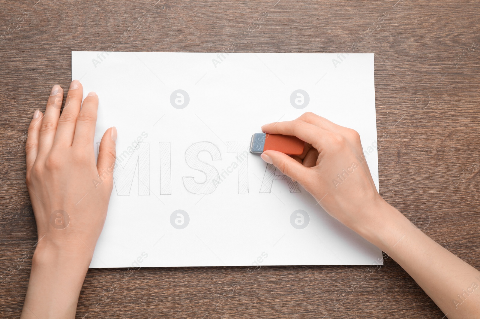 Photo of Woman erasing word on sheet of white paper at wooden table, top view