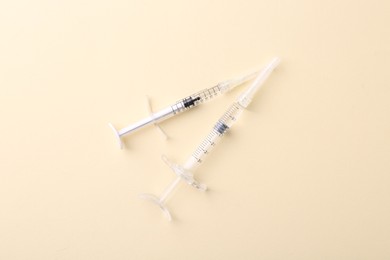 Photo of Injection cosmetology. Two medical syringes on beige background, top view