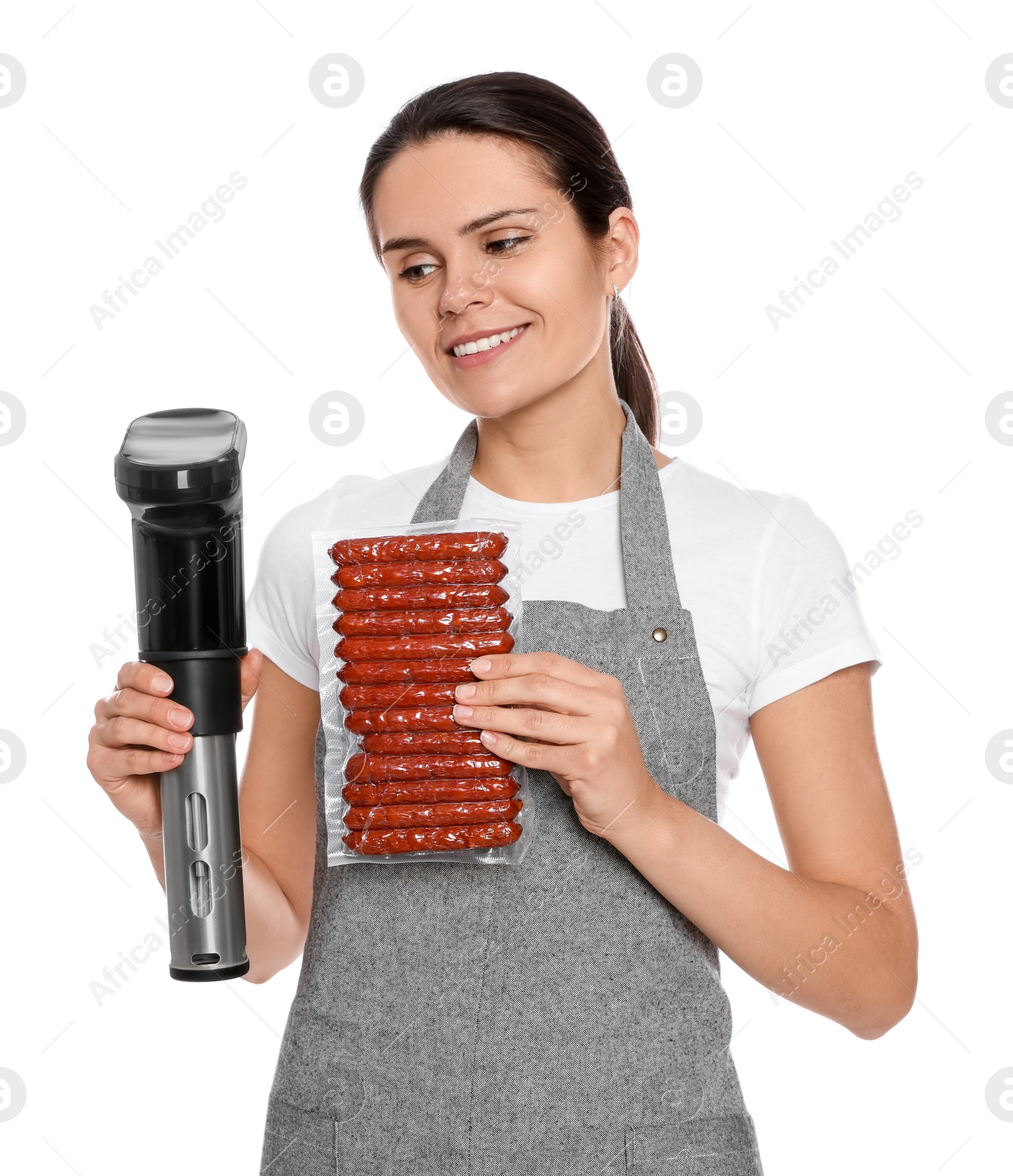 Photo of Beautiful young woman holding sous vide cooker and sausages in vacuum pack on white background