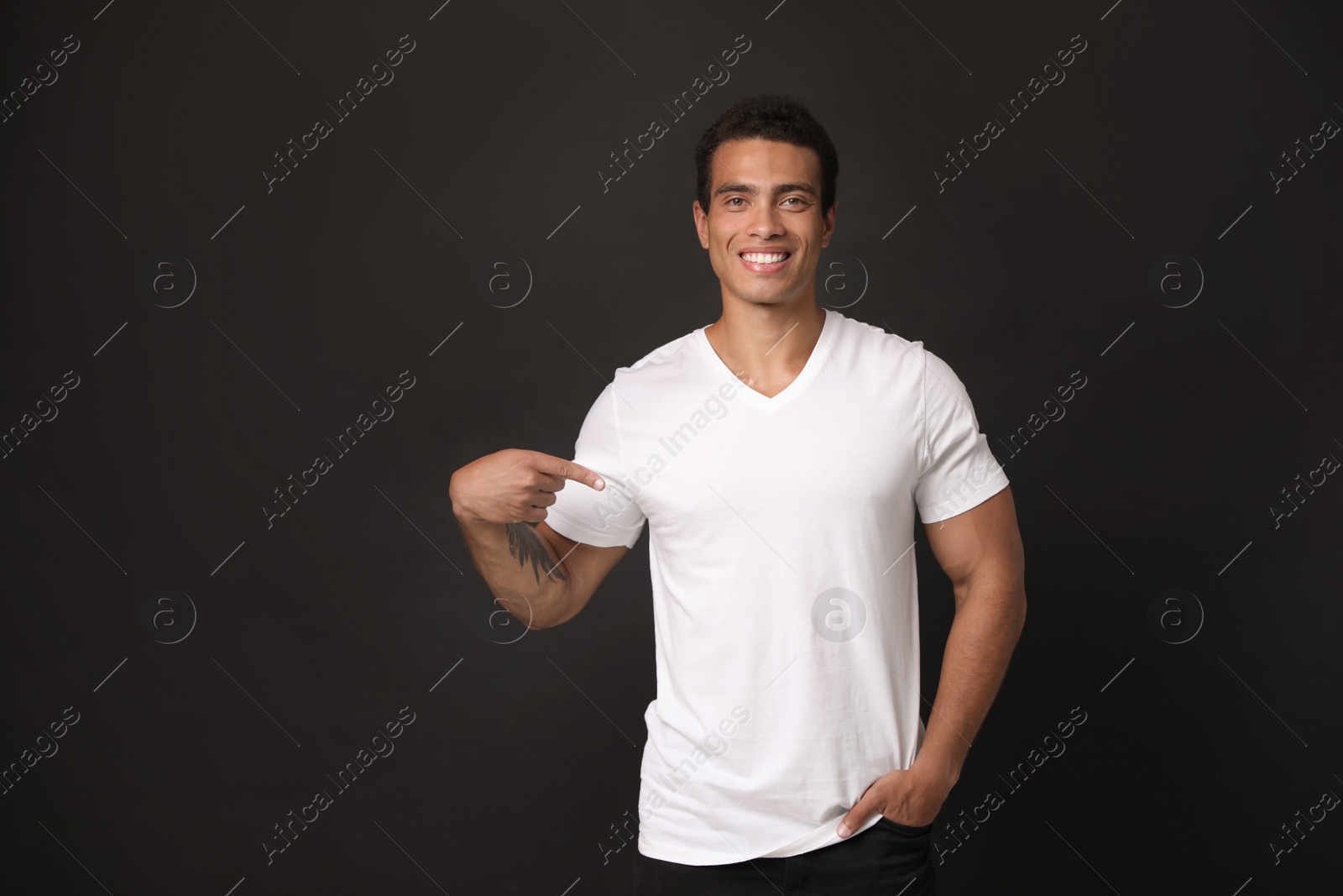 Photo of Handsome young African-American man in blank t-shirt on black background. Space for design