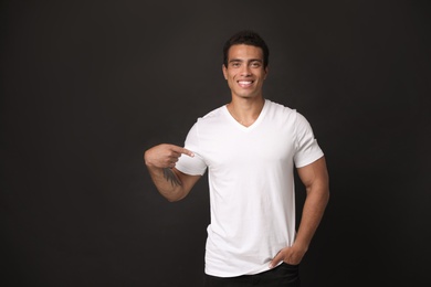 Handsome young African-American man in blank t-shirt on black background. Space for design