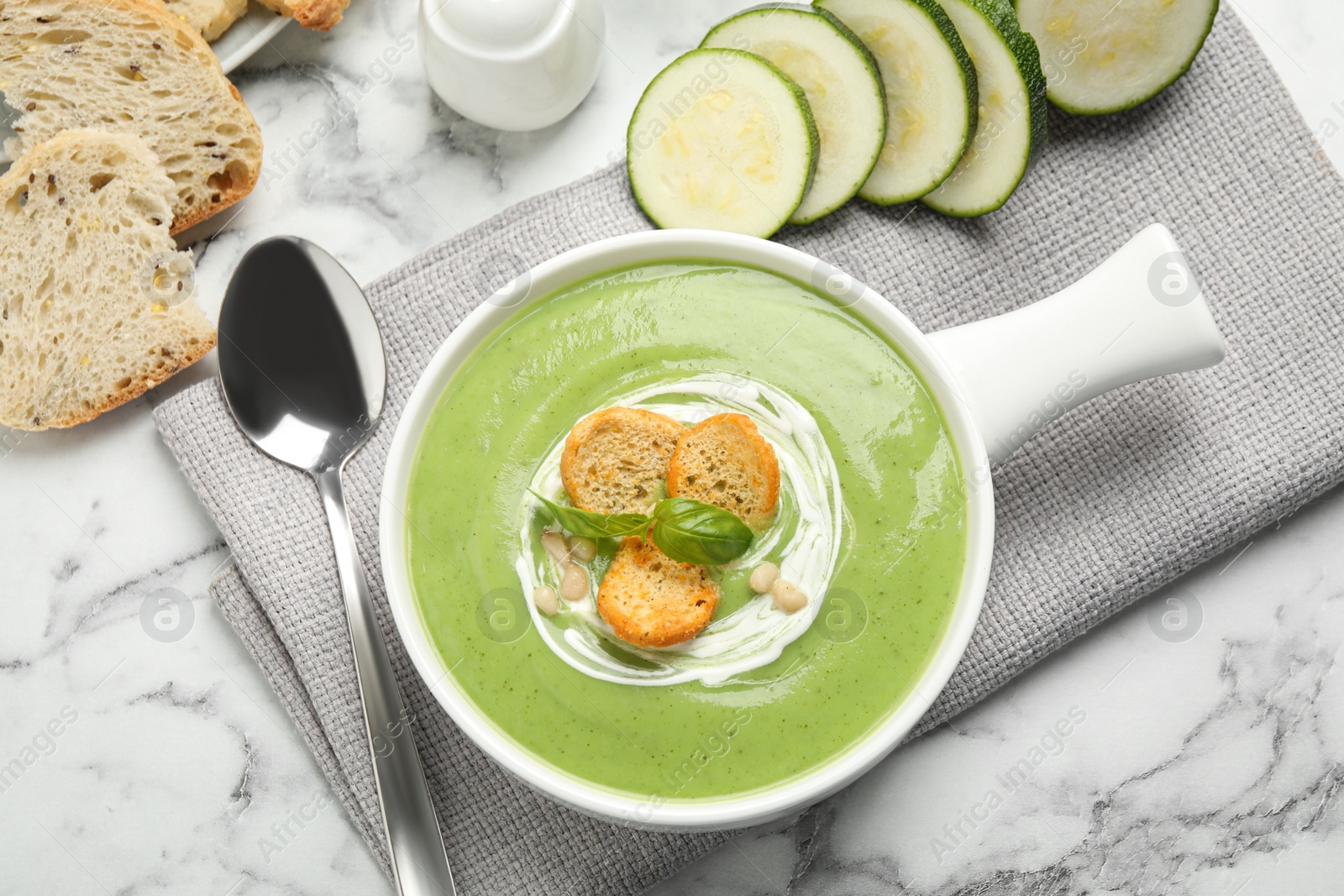 Photo of Tasty homemade zucchini cream soup served on marble table, flat lay