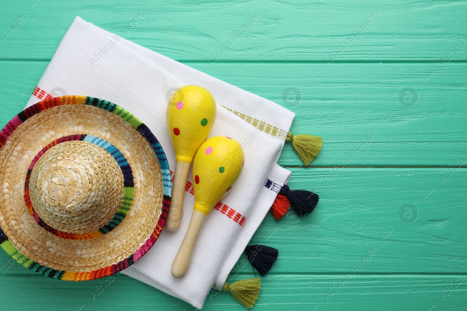 Photo of Mexican sombrero hat, maracas and poncho on turquoise wooden table, flat lay. Space for text