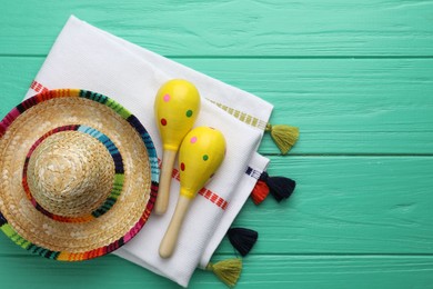 Photo of Mexican sombrero hat, maracas and poncho on turquoise wooden table, flat lay. Space for text