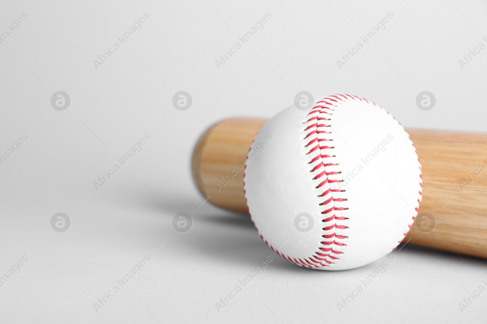 Photo of Wooden baseball bat and ball on light grey background, space for text. Sports equipment