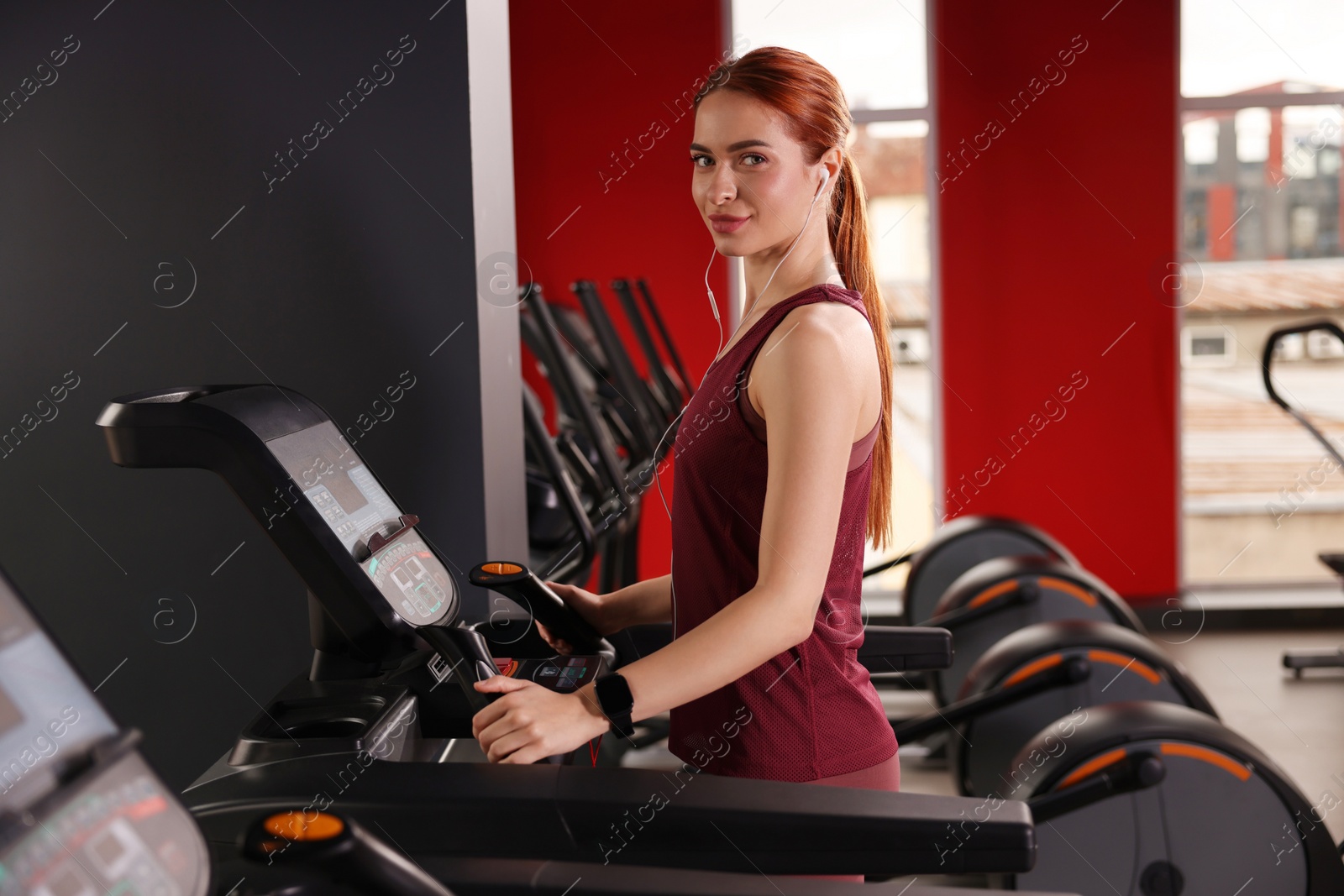 Photo of Athletic young woman with earphones training on treadmill in gym