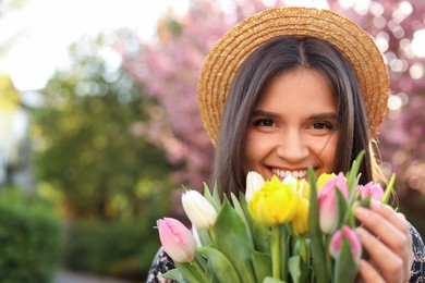 Photo of Beautiful young woman with bouquet of tulips in park on sunny day, space for text