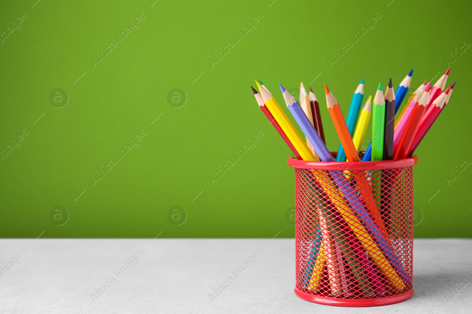 Photo of Many colorful pencils in holder on light table against green background, space for text