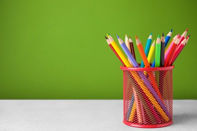 Many colorful pencils in holder on light table against green background, space for text