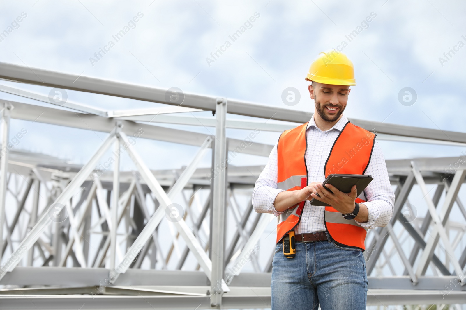 Photo of Professional engineer with tablet near high voltage tower construction outdoors. Installation of electrical substation